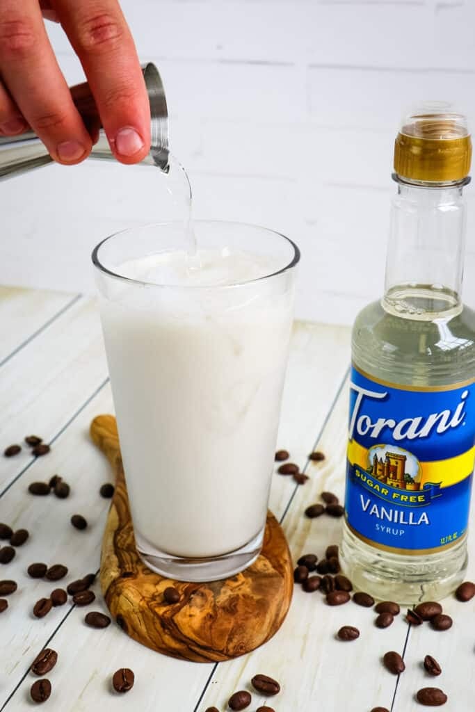 Vanilla syrup being poured into a glass with milk and ice to make an iced vanilla latte recipe.