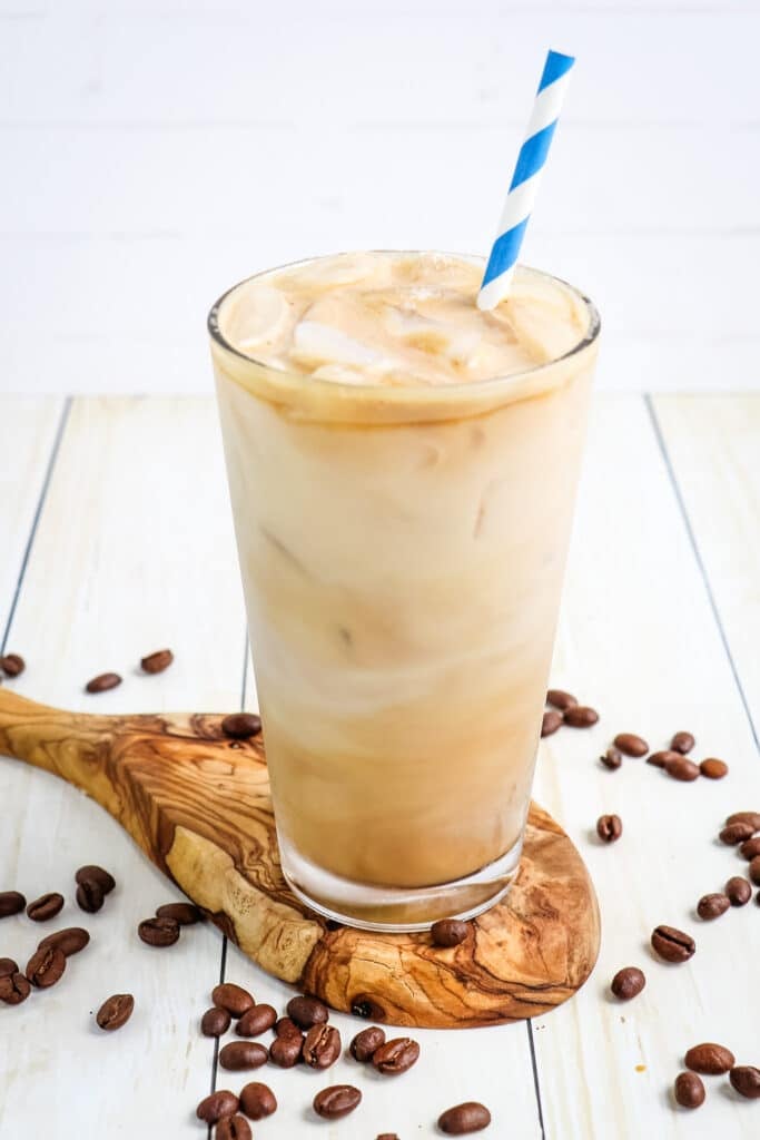 Iced skinny vanilla latte with coffee beans on the side and blue striped straw.