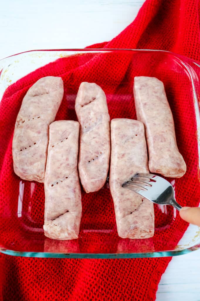 Brats being pierced with a fork before cooking.