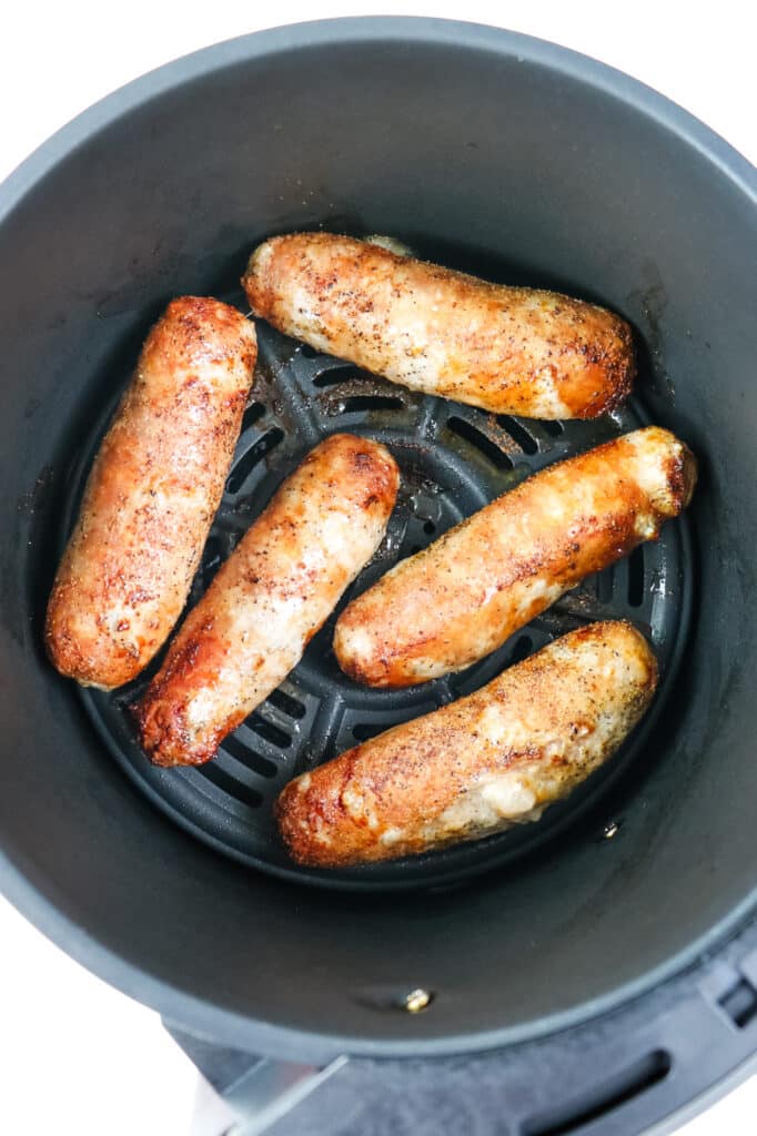Five cooked brats in air fryer basket.