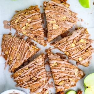 Baked apple cinnamon scones on a lined baking sheet topped with drizzled cinnamon glaze.