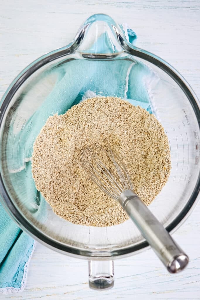 Dry ingredients for banana protein muffins in a mixing bowl with a whisk in the center.