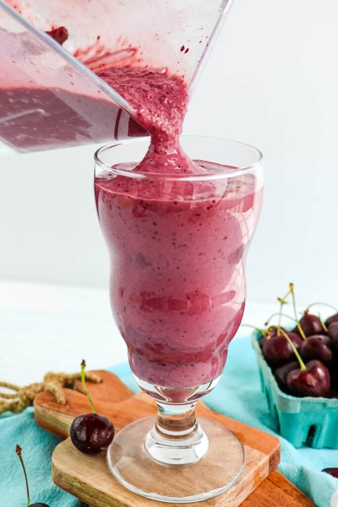 Cherry milkshake being poured into a tall milkshake glass.