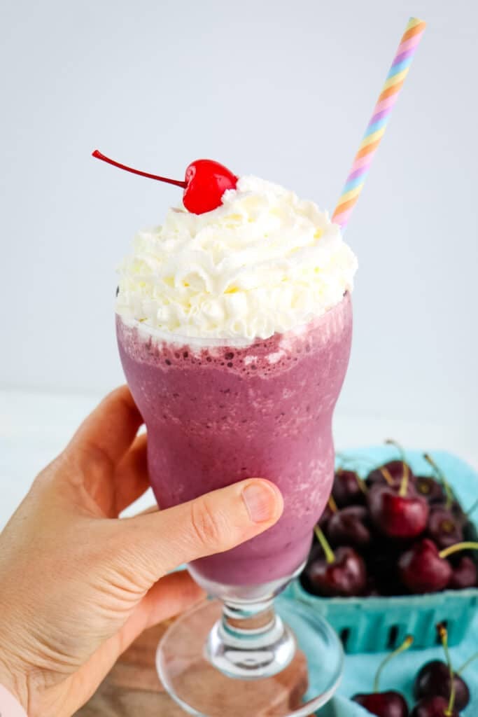 Cherry milkshake being held in hand with a striped straw.