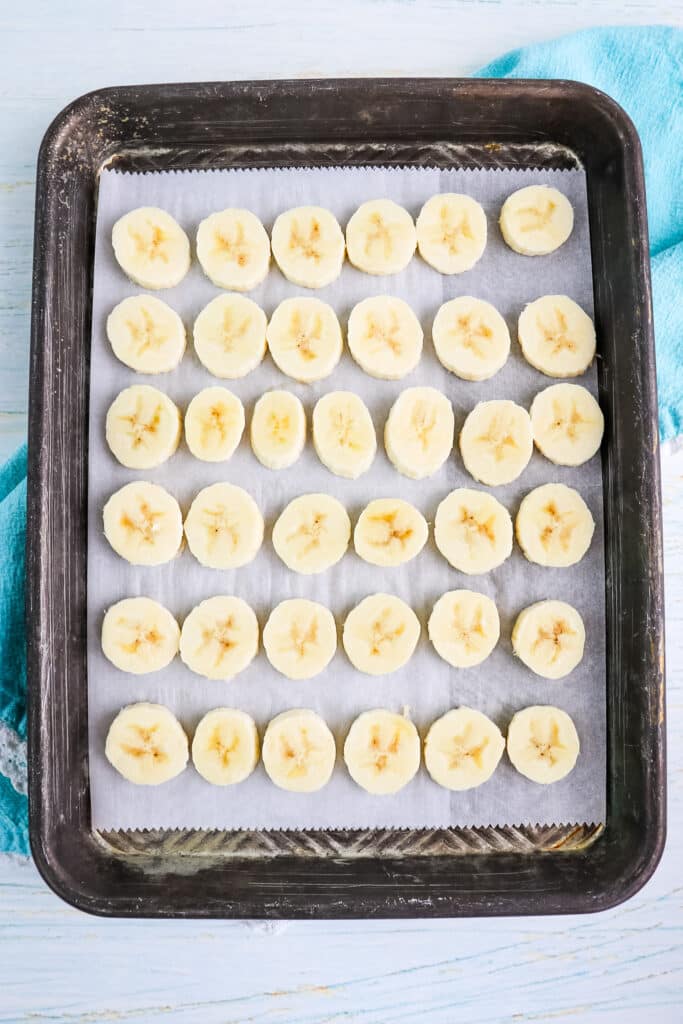 Banana slices on a sheet pan to be frozen for making peanut butter banana bites.
