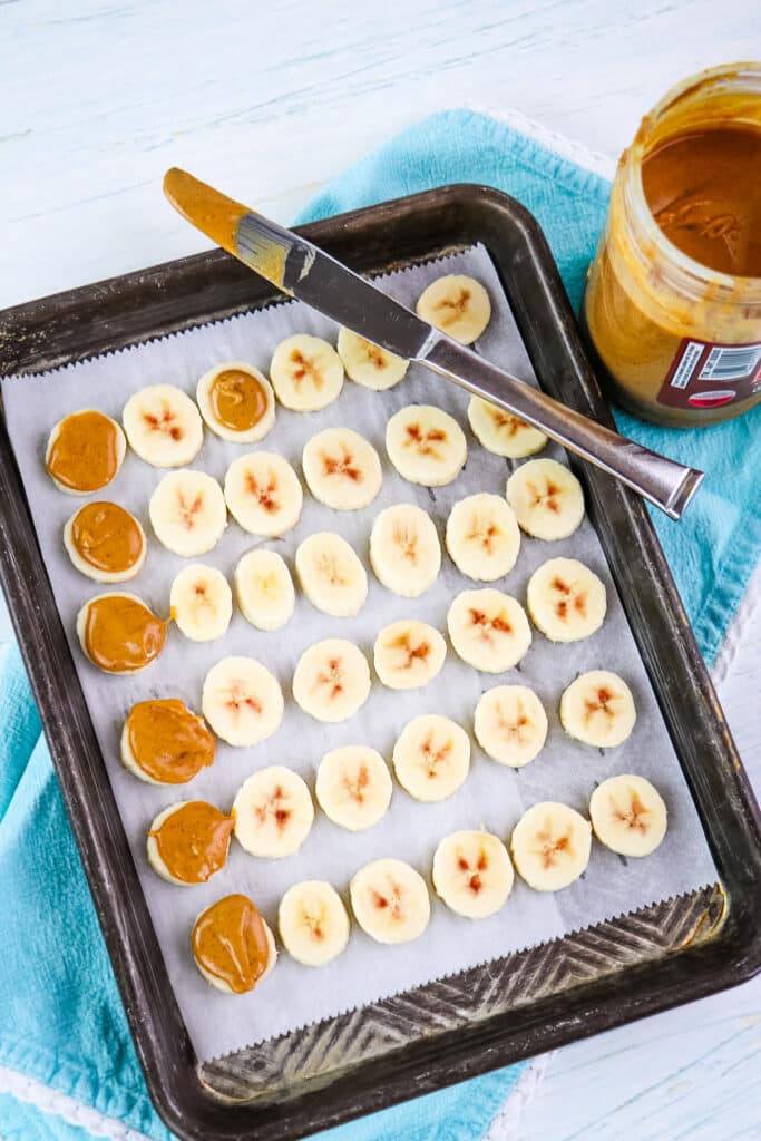 Peanut butter being added to tops of banana slices to make chocolate covered banana bites.