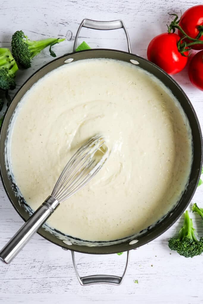 Homemade alfredo sauce in a large skillet with whisk in the center of the pan.