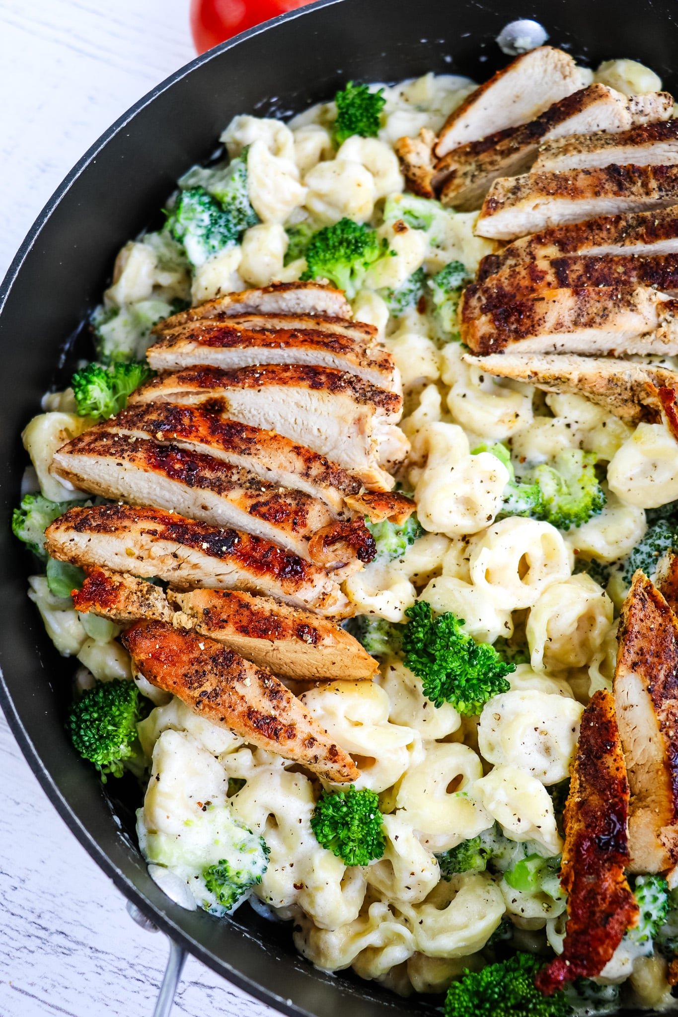 Tortellini alfredo recipe topped with sliced chicken breasts.