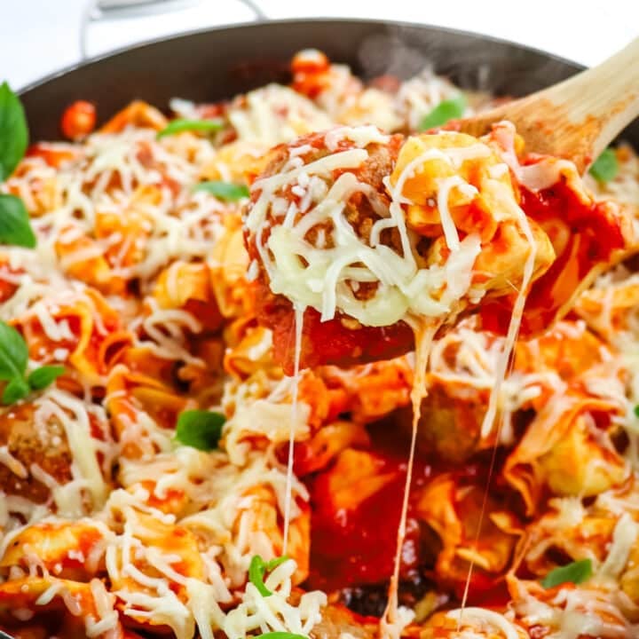 Cheese tortellini and meatball marinara topped with melted mozzarella cheese with spoon taking helping out with cheese pulls coming off the spoon.