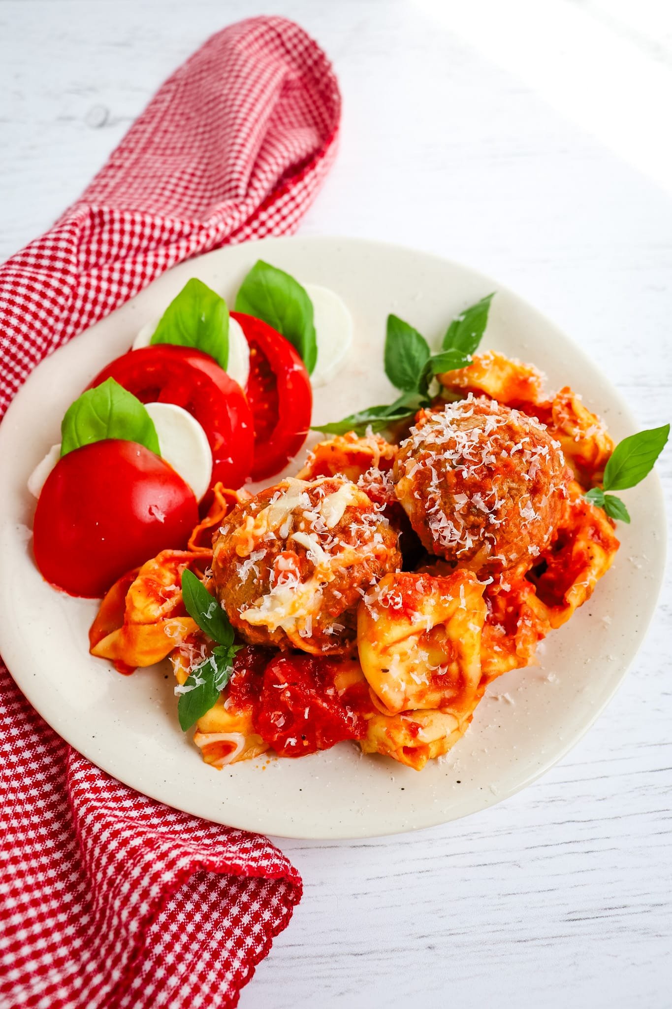 Tortellini and meatball marinara garnished with fresh basil leaves and caprese salad on the side.