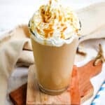 Starbucks caramel frappuccino recipe topped with whipped cream and caramel sauce in a tall, clear glass.