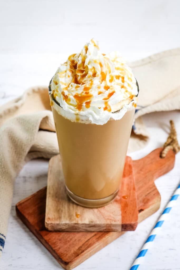 Starbucks caramel frappuccino recipe topped with whipped cream and caramel sauce in a tall, clear glass.
