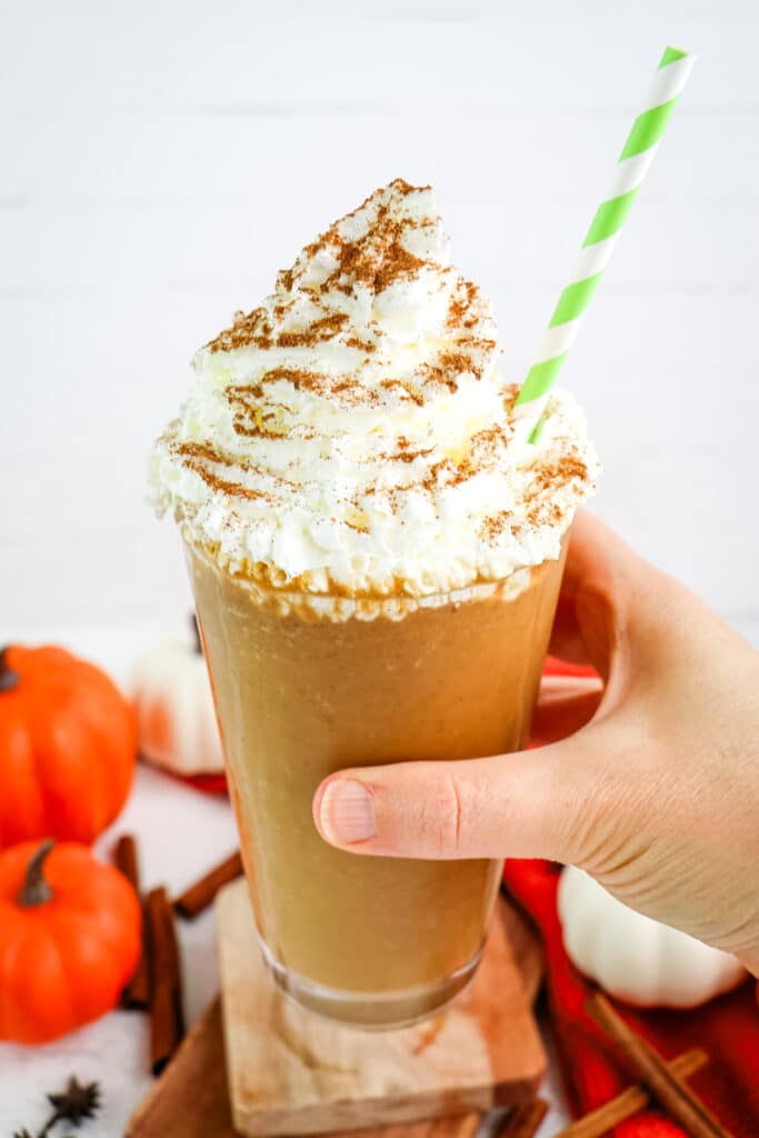 A pumpkin spice frappuccino being held in hand with a striped green straw.