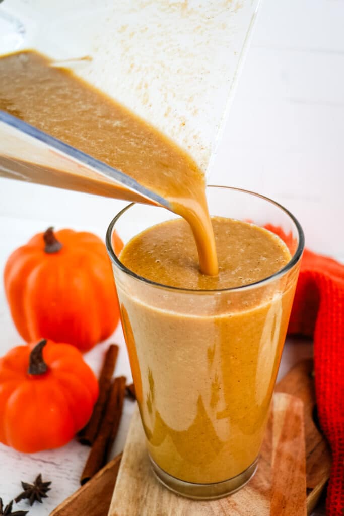 A blended pumpkin spice frappuccino being poured from the blender into a tall glass.