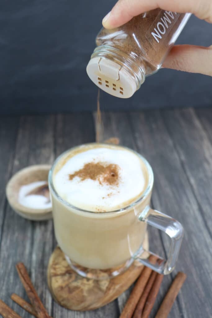 Cinnamon being sprinkled over the top of a latte.