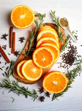 Ingredients needed to make a citrus turkey brine, with sliced oranges in the center and rosemary sprigs on the side.