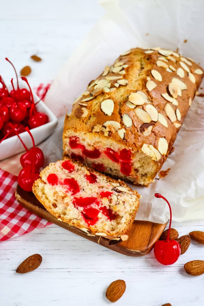 Loaf of maraschino cherry bread that has once slice on its side. 