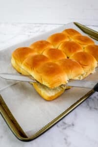Hawaiian rolls being sliced in half with a long serrated knife.