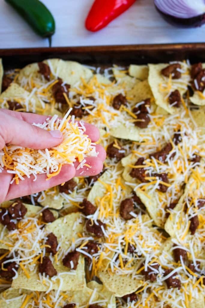 Shredded cheese being added to tortilla chips and steak for making a steak nacho recipe.