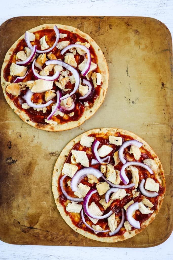 Sliced red onion sprinkled on two bbq chicken flatbreads.