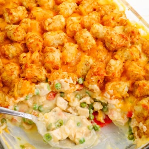 Tater tot casserole with chicken in a glass baking dish with spoon in the center.