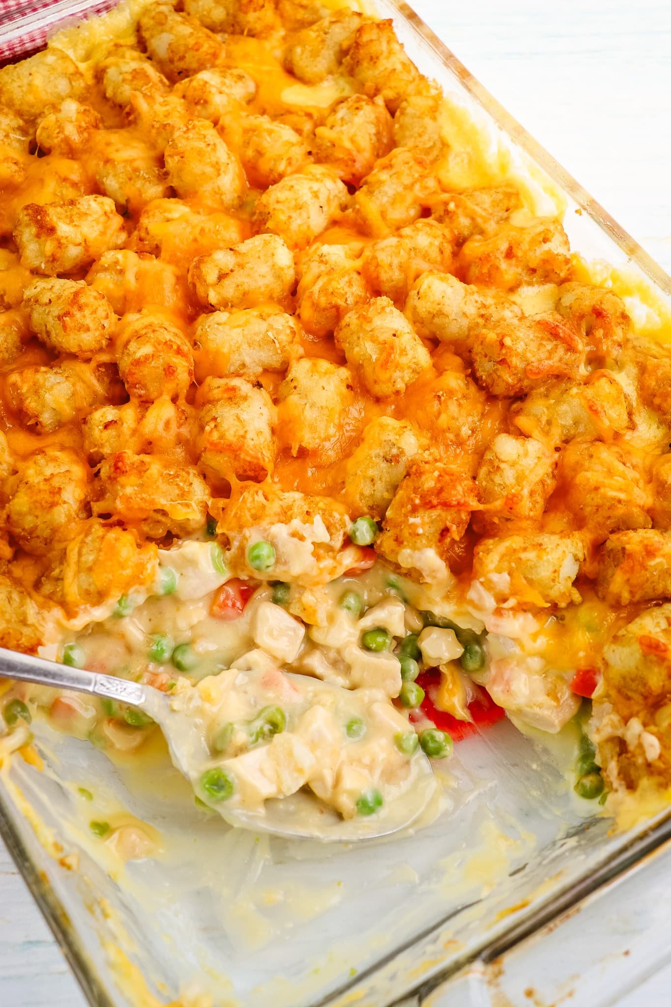 Tater tot casserole with chicken in a glass baking dish with spoon in the center.