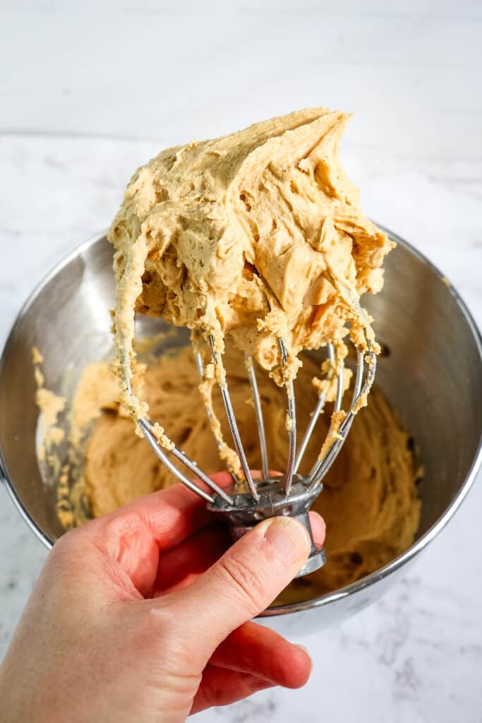 Peanut butter frosting on a whisk attachment over a mixing bowl.