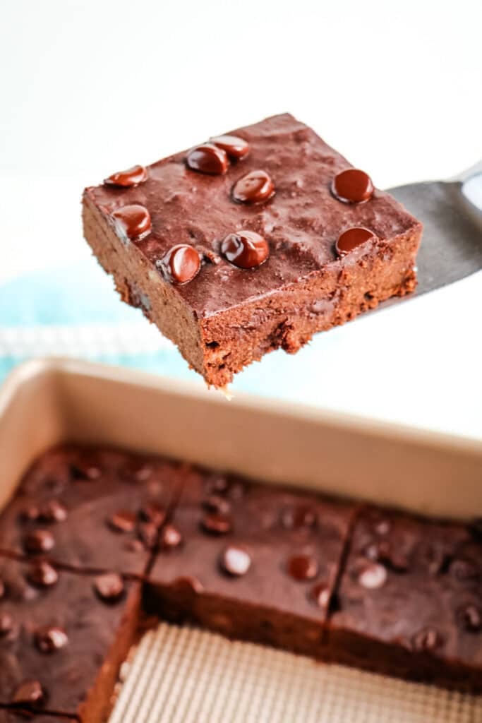 Banana brownies cut into squares with one brownie being lifted out of pan on a spatula.