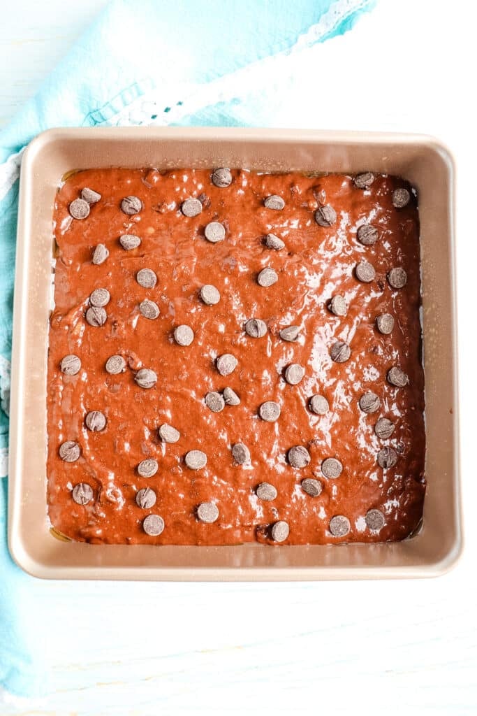 Brownie batter spread into a square pan and topped with chocolate chips.