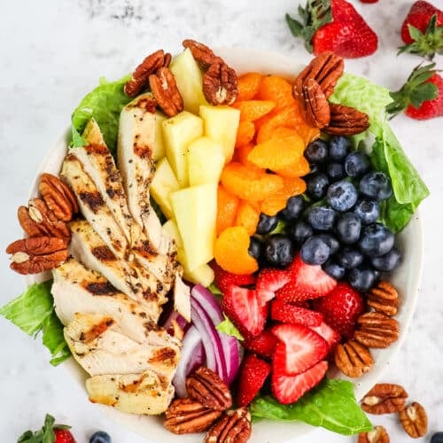 A Panera strawberry poppyseed salad with pecans, berries, pineapple, oranges and grilled chicken in a bowl.