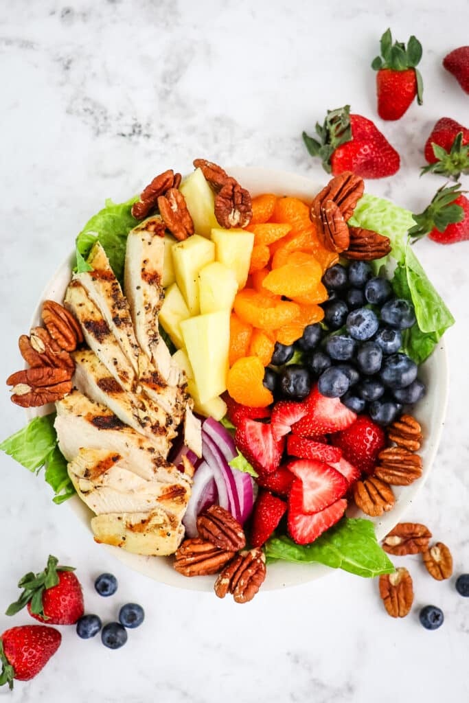 A Panera strawberry poppyseed salad with pecans, berries, pineapple, oranges and grilled chicken in a bowl.