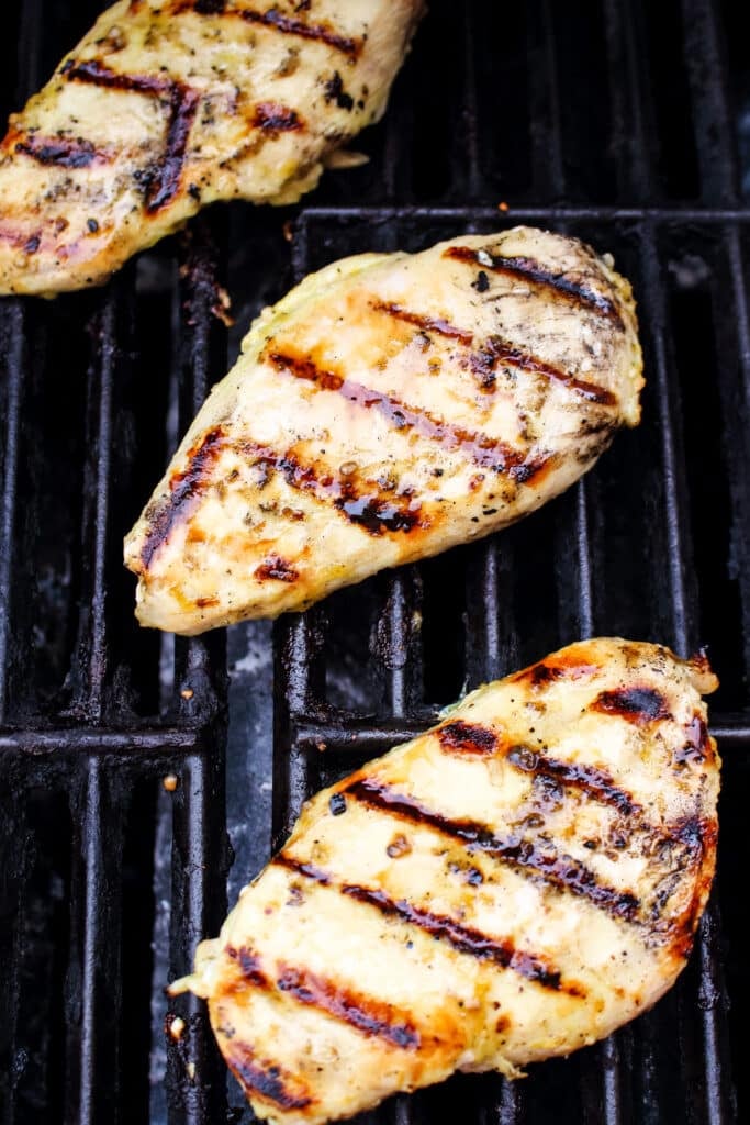 Lemon pepper grilled chicken being cooked on grill grates.