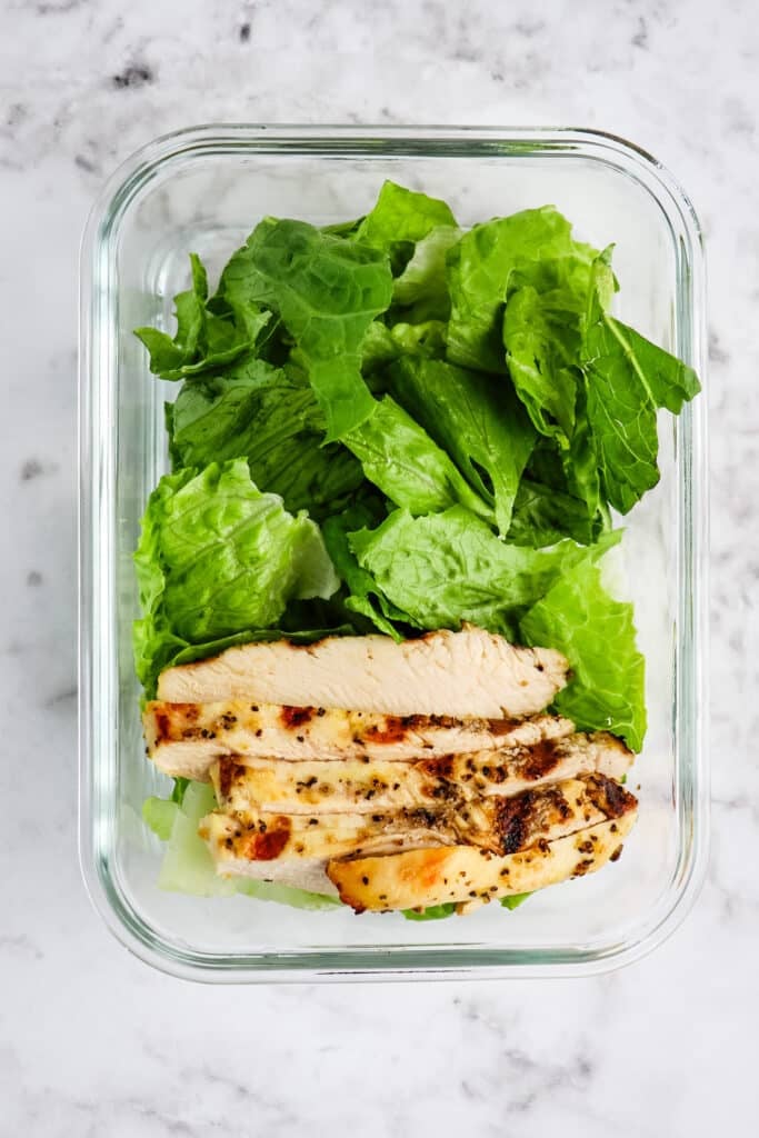 Glass meal prep container with romaine lettuce and grilled chicken for prepping strawberry poppyseed salad.