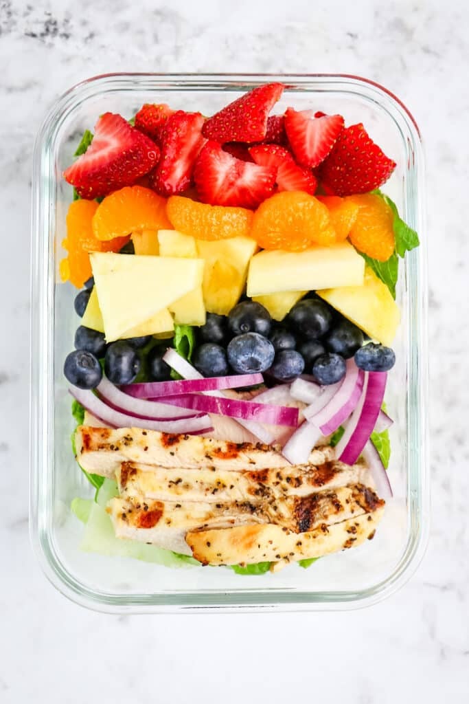 A strawberry poppyseed salad with chicken, red onions, blueberries, pineapple, oranges and strawberries.