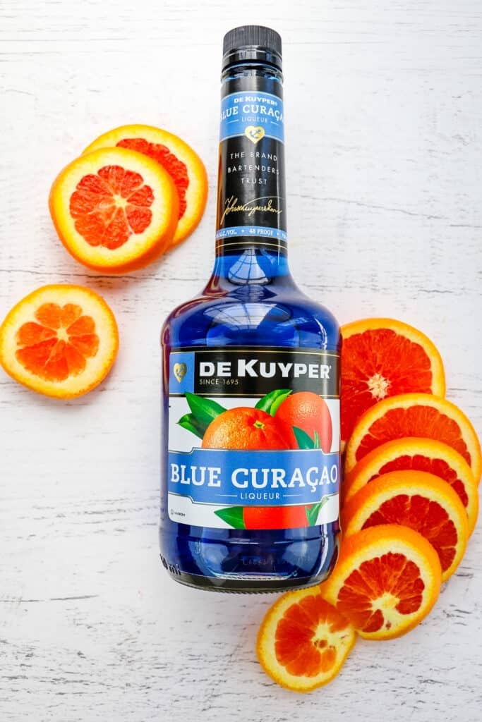 Bottle of blue curacao liqueur with sliced cara cara orange on the side.