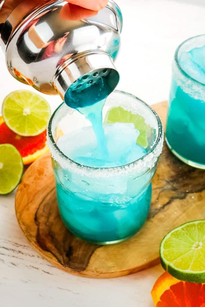 A blue margarita being poured into a salted glass.