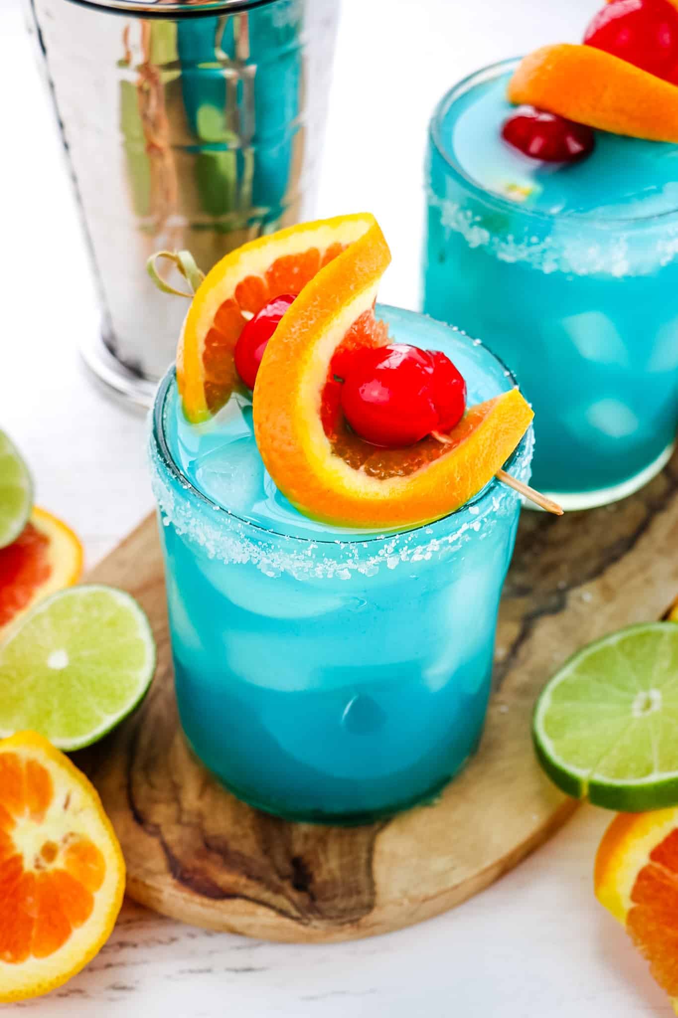 Blue margaritas topped with orange slice and cherry garnished with salt on the rims of the glasses.