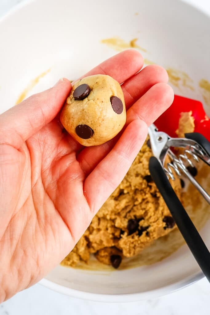 Cookie dough protein balls being formed, with one ball in a hand.