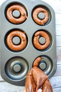 Chocolate cake batter being piped into a donut pan.