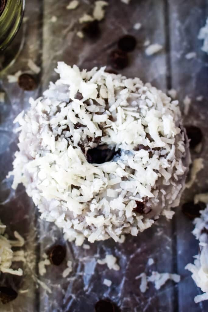 A single coconut chocolate donut with coconut sprinkles garnished on the side.