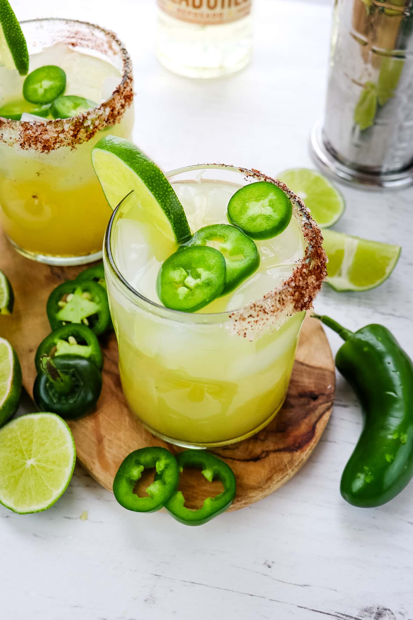 Jalapeno margarita recipe in two glasses garnished with lime and jalapeno slices and a salted rim with chili powder.
