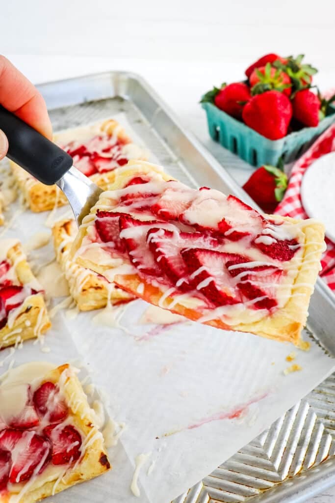 Strawberry Danish being lifted off a sheet pan with a spatula.