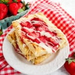 Three Strawberry cream cheese Danish on a white plate with fresh strawberries in the background.