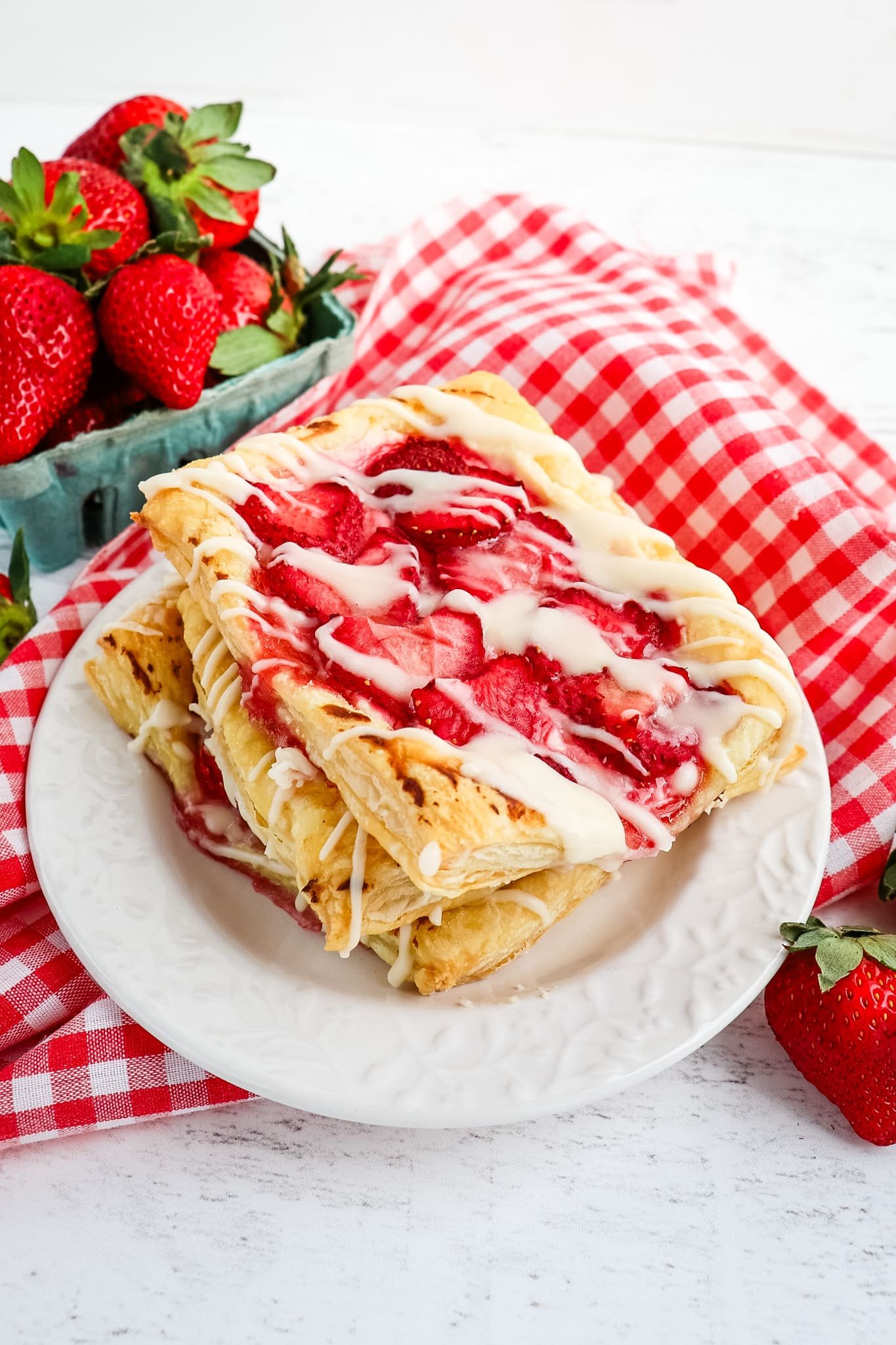 Three Strawberry cream cheese Danish on a white plate with fresh strawberries in the background.