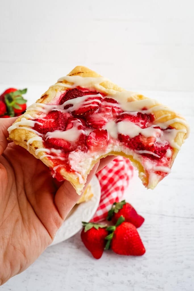 Strawberry Danish held in hand with a single bite taken out.