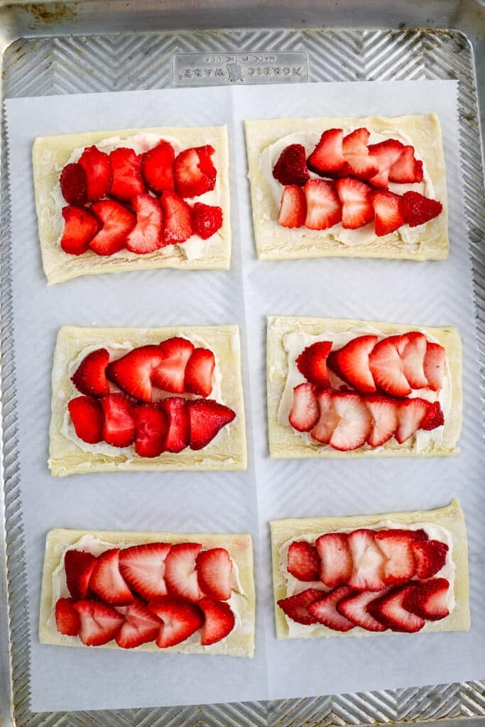 Sliced strawberries on top of cream cheese and puff pastry on a baking sheet before being baked.