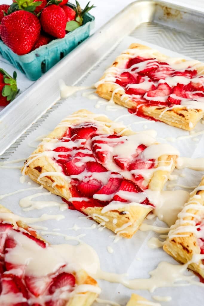 Close up of a strawberry cream cheese puff pastry topped with a drizzle of glaze with fresh strawberries in the background.