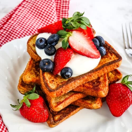 Stack of healthy French toast on a white plate topped with Greek yogurt and fresh berries.