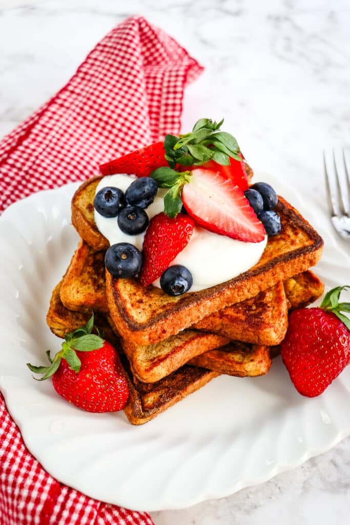 Stack of healthy French toast on a white plate topped with Greek yogurt and fresh berries.