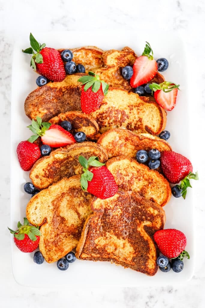 Several slices of healthy French toast on a white platter garnished with strawberries and blueberries.